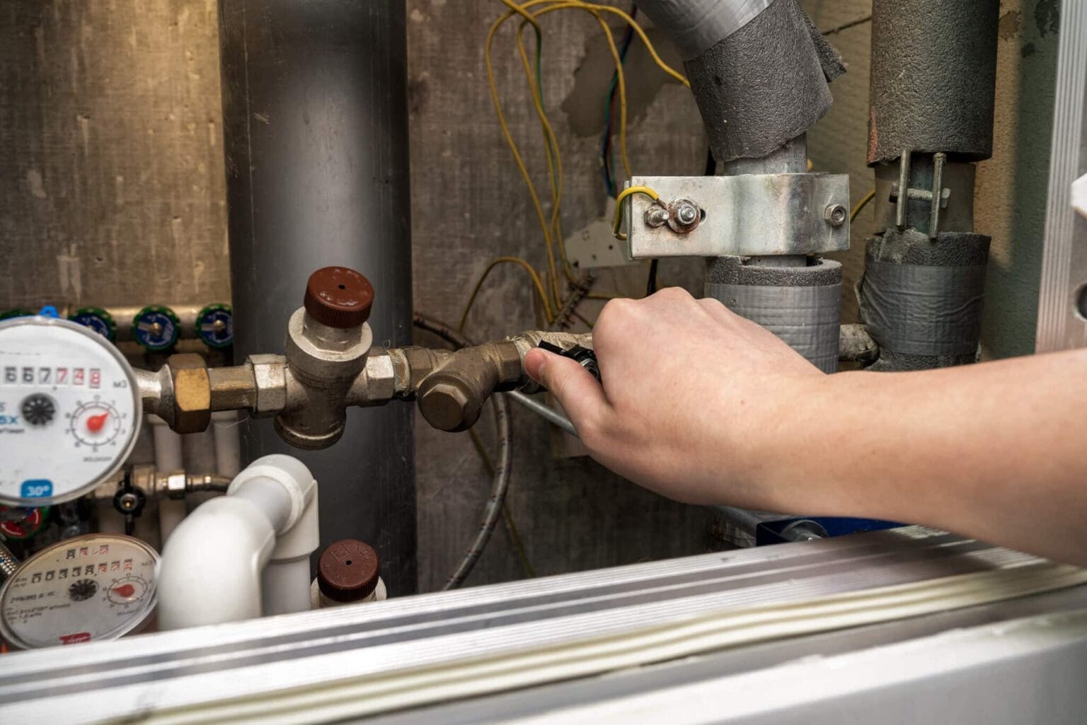 Hånd justerer rørventil i teknikrum